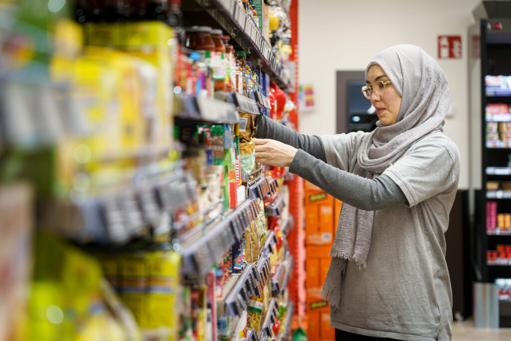 Eine Dame mit Kopftuch schlichtet Waren in eine Supermarktregal 