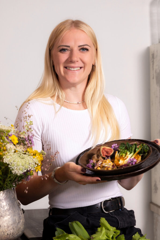Eine Blonde Frau hält einen Teller mit Essen in die Kamera