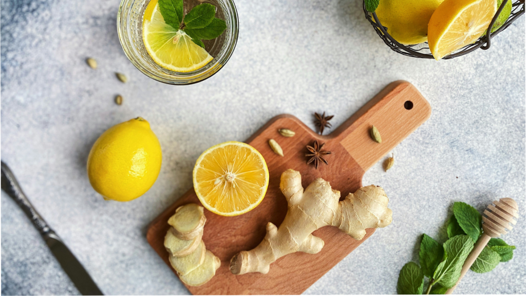 Ingwer und Zitronen auf einem Schneidebrett neben Gläsern.