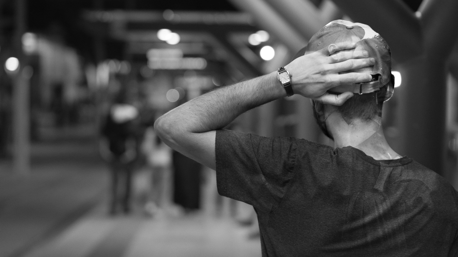 schwarzweiß foto von einem Mann von hinten, der sich auf den Hinterkopf greift