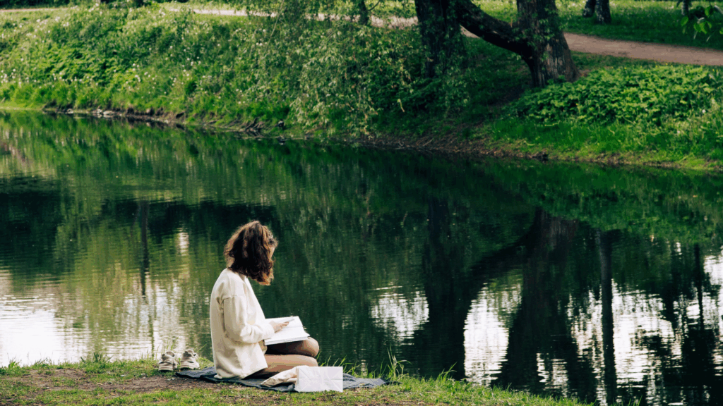 Eine Frau sitzt auf einer Wiese am Wasser und liest