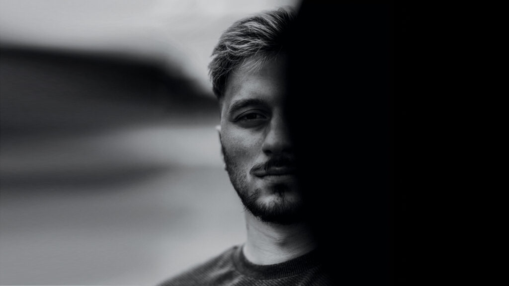 Femizid: Schwarz-Weiß-Porträt eines Mannes, dessen Gesicht zur Hälfte im Schatten liegt, als Symbolbild für Gewalt und Bedrohung.